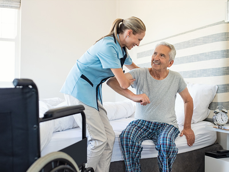 Caregiver helping older man get out of bed in the morning at home